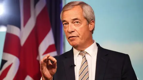PA Media Nigel Farage pictured wearing a dark suit, striped tie and white shirt. He is standing in front of a union jack.