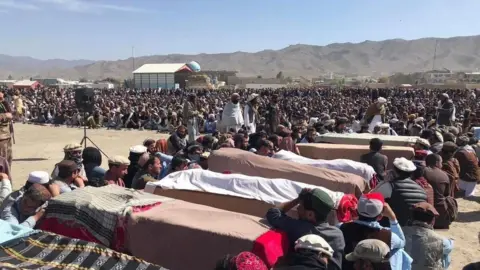 Several coffins laid out in front of a large outdoor crowd in Afghanistan