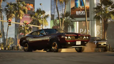 Build a Rocket Boy Screenshot from MindsEye shows a burgundy muscle car in the middle of an American-style street flanked by tall buildings. Dust billows from the vehicle's tyres, and the suspension on the driver's side sits low, suggesting a sharp corner turn.