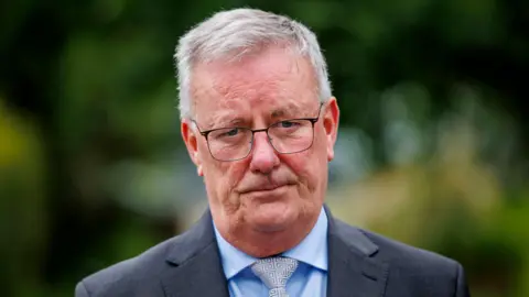 PA Media Health Minister Mike Nesbitt, pictured from the shoulders up, wearing a grey suit, blue shirt and grey tie. He is also wearing glasses and has short grey hair. 