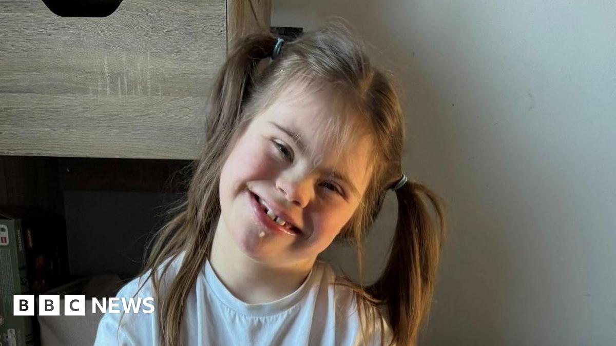 A young girl wearing a white t-shirt and her hair in ponytails smiles happily