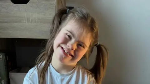 Family photo A young girl wearing a white t-shirt and her hair in ponytails smiles happily