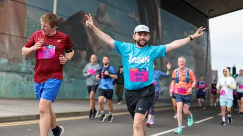 Great Scottish Run a runner wearing a blue "SAMH" shirt and a white cap, makes peace signs with both hands.