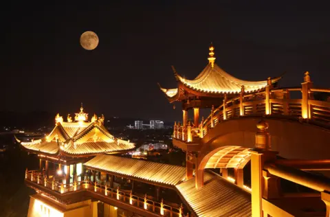 Getty Images The full supermoon against a dark night sky, floating above a well-lit, ornately designed pavilion in Jinhua, Zhejiang Province.