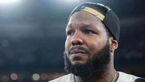 Getty Images  Toronto Blue Jays first baseman Vladimir Guerrero Jr. (27) is emotional after the game as the Toronto Blue Jays play the Seattle Mariners in game seven of their ALCS MLB Playoff series at Rogers Centre in Toronto. October 20, 2025. He is wearing a black baseball cap backwards and a white Blue Jays jersey. The photo is taken from a low angle, focusing on his face as he looks out at the crowd.