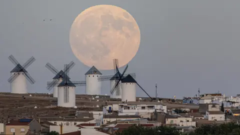 EPA A massive supermoon hovers above windmills on a hill in Ciudad Real, Spain, in the early evening sky