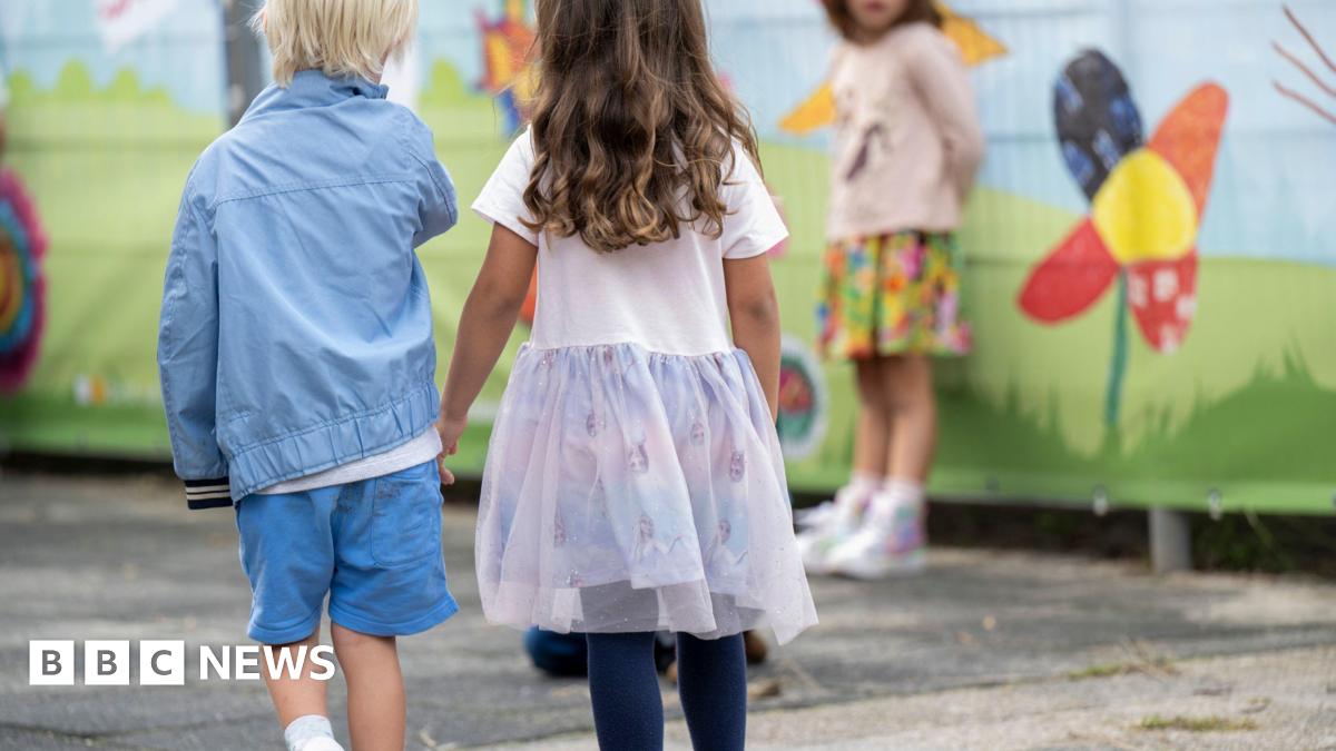 The back of two small children standing in a playground.