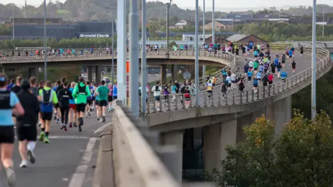 Great Scottish Run a large group of runners taking part in a race on an elevated roadway, with bright athletic gear and city scenery in the background.