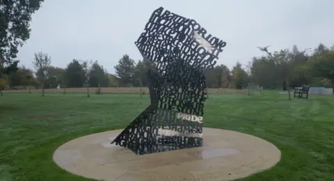 Gemma Laister/BBC News The memorial, which is made of copper, and has words such as 'pride', 'resilience', and 'a battle for love'