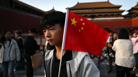 Getty Images A man holds a Chinese flag in front of the Forbidden City in Beijing during China's National Day Golden Week holiday