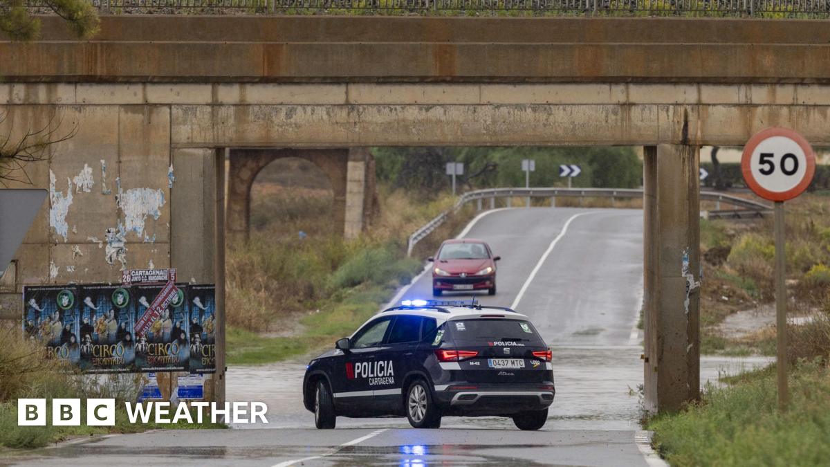 Police car parked in centre of road next to road obscured by flood water