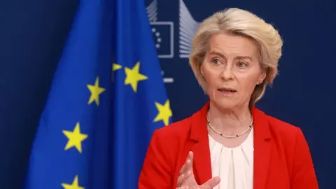EPA/Shutterstock Von der Leyen wears a red jacket and white blouse with the blue and yellow flag of the EU in the background
