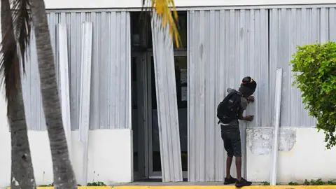 Getty Images A man installs metal storm shutters on the front of a building