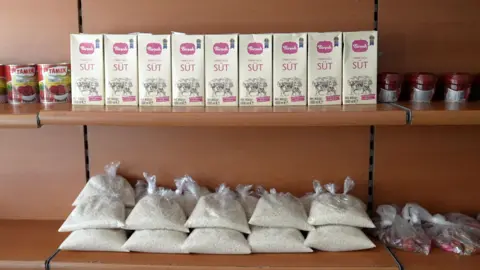 Shelves with bags of rice, tins of tomatoes and cartons of milk.