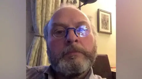 Facebook A selfie style photo of a bearded man in glasses at home