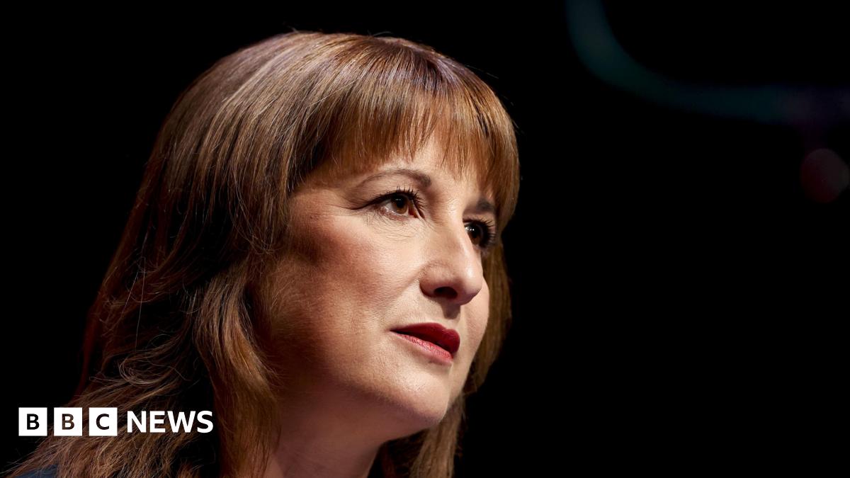 A close up of the chancellor pictured from the right hand side, she has a serious neutral expression on her face, which is framed by her brown hair - she is looking off into the distance and her face appears to be lit by stage lights