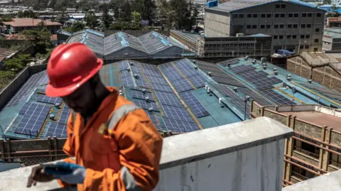 AFP via Getty Images A technician from CP Solar works on the installation of solar panels at the roof a partially solar-powered factory in the industrial area of Nairobi. Renewable energy sources generate over 80 percent of Kenya's electricity.  