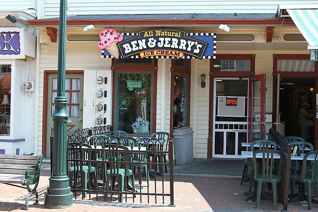 Exterior of a Ben & Jerry’s ice cream shop with outdoor seating and a sign reading “All Natural Ben & Jerry’s Ice Cream.”