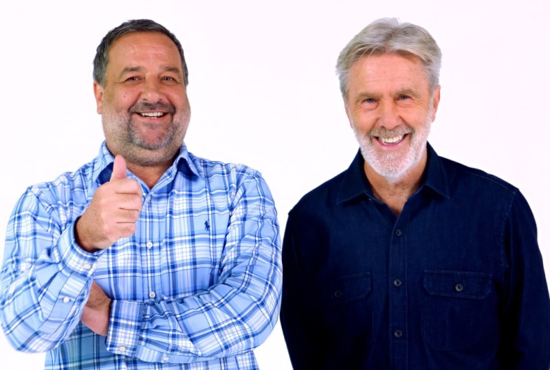 Two smiling middle-aged men standing side by side against a white background. One man, wearing a blue plaid shirt, gives a thumbs up, while the other, dressed in a dark shirt, smiles broadly. This image conveys a sense of positivity and camaraderie.