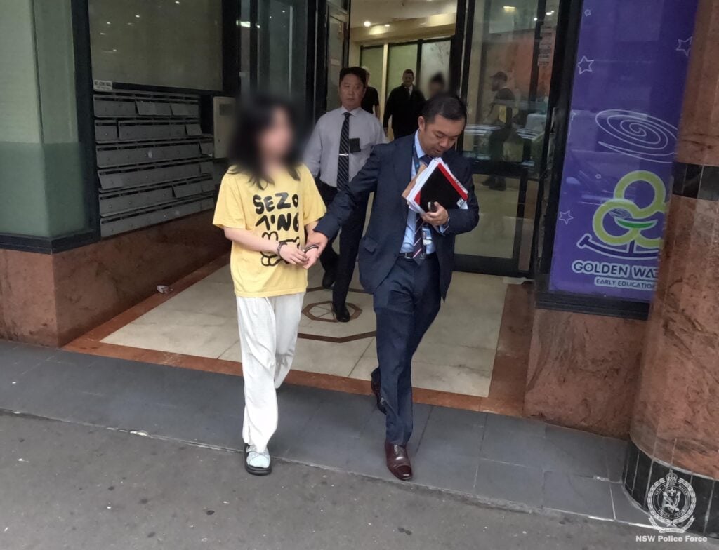 A male detective in a dark blue suit walking a woman in a yellow shirt