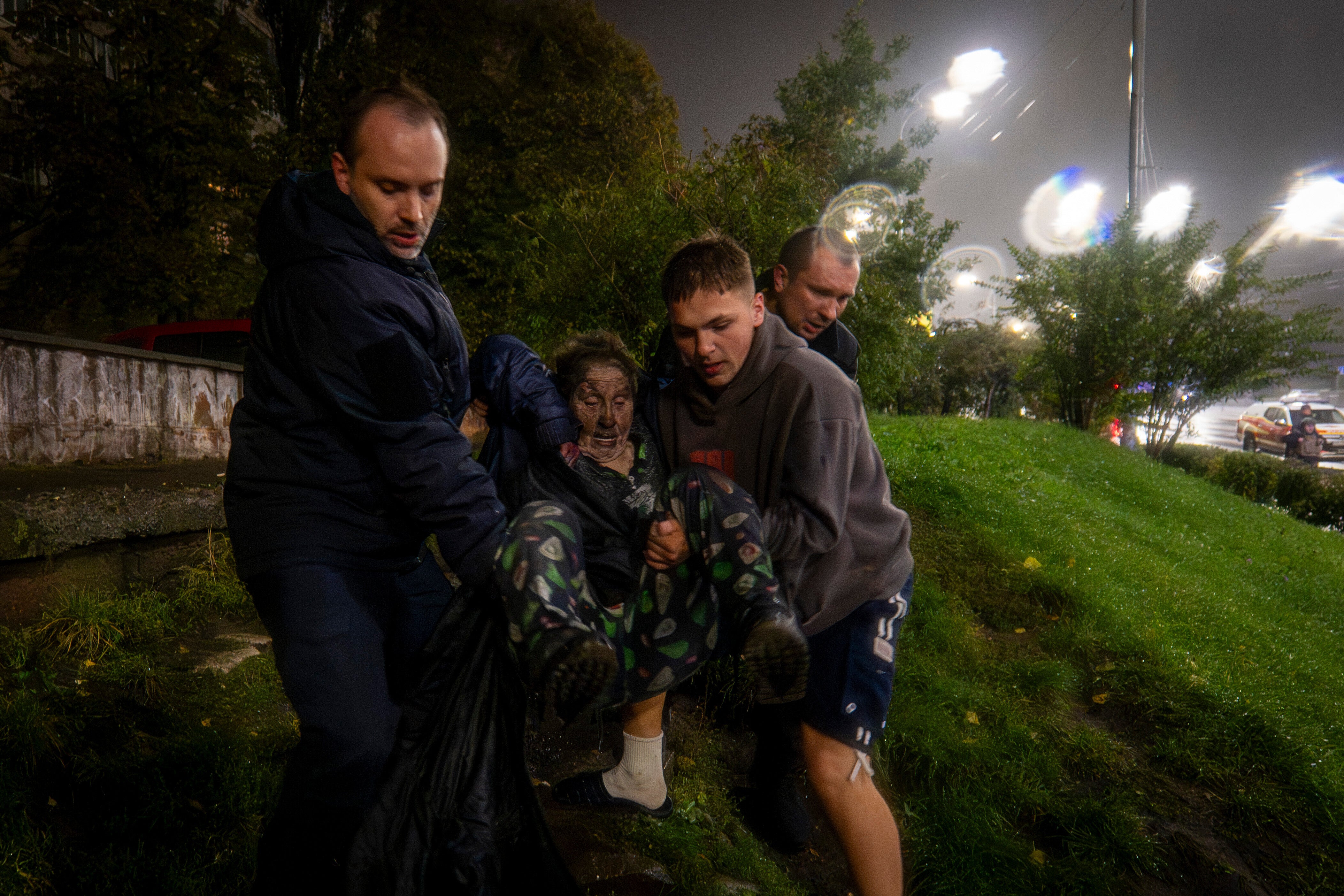 Neighbors carry an injured woman to safety following the shelling of an apartment block in Kyiv