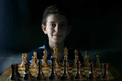 Getty Images A young Daniel Naroditsky sitting behind a chessboard 