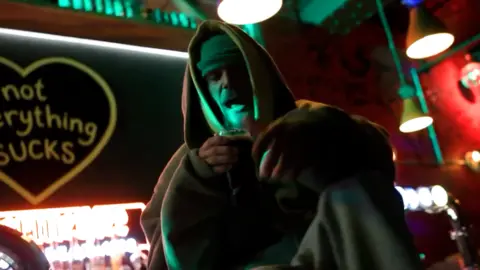 Justin Bieber/Instagram Justin Bieber in a hat and hooded top, appears to sit on top of a bar. He has a pint in his hand. A very dark picture.