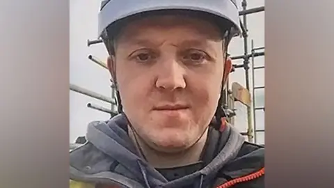 Police Scotland A man looking into the camera while wearing a light blue or grey hard hat, seemingly on a building site. 