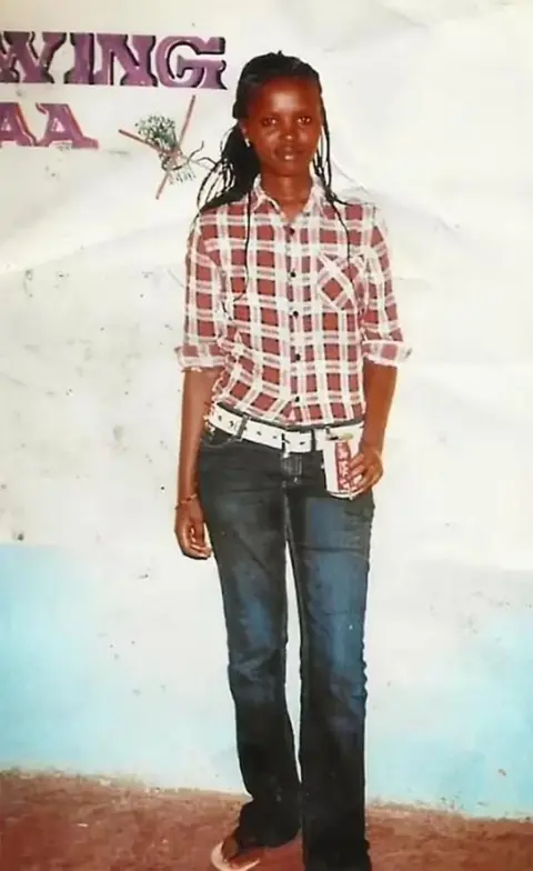 Wanjiru Family A full-body photo of Agnes Wanjiru wearing jeans and a chequered shirt
