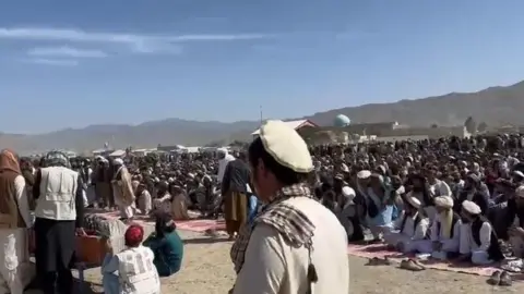 BBC A large crowd of likely hundreds of people seen outside beside mountains