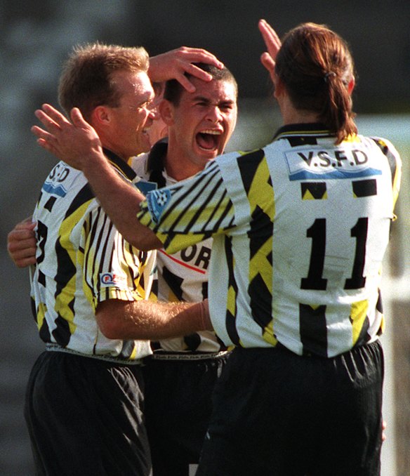 Rick Cerrachio (centre) celebrates a goal for the Collingwood Warriors with Mark Silic (left) and Goran Lozanovski (right).