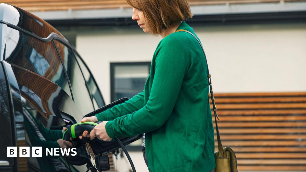 Woman wearing a green jumper plugging a charging cable into a black electric vehicle