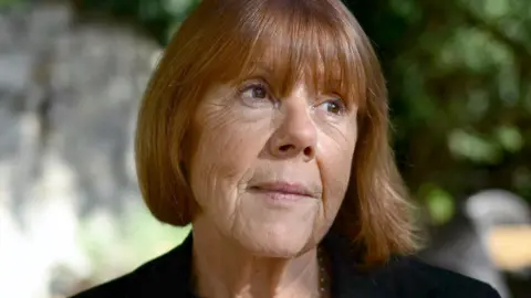 Getty Images Gisèle Pelicot, a woman with chestnut hair in a bob, pictured in the dappled light of a garden or park, in close-up, looking up and to the left, with the background blurred behind her
