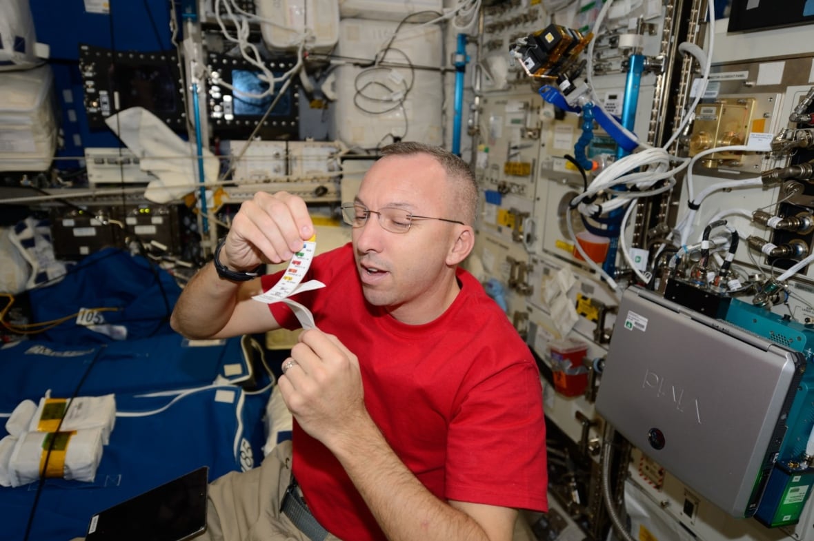 A man in a red shirt sits in weightlessness holding open a small booklet of paper.