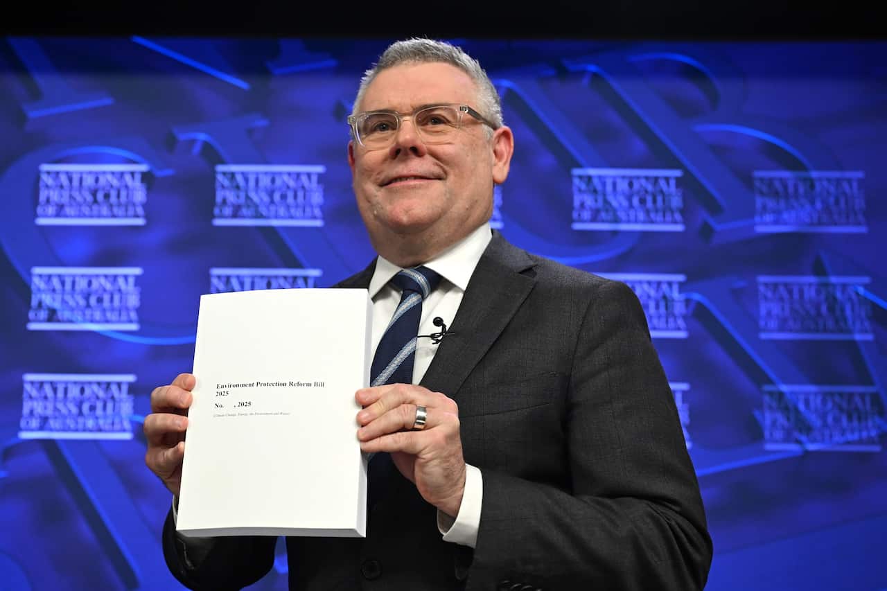 Environment Minister Murray Watt stands in front of a blue wall at the National Press Club in Canberra holding the almost 1,500 page Environment Protection Reform Bill.
