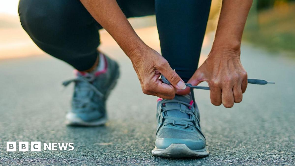A stock image close-up of a female athlete tying her running shoe.