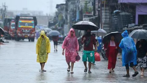 Getty Images People in colourful raincoats, others with umbrellas, walking on a road in heavy rain