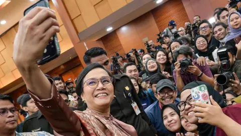 Getty Images Former Indonesian Finance Minister Sri Mulyani Indrawati takes a selfie with journalists after the handover ceremony to her successor Purbaya Yudhi Sadewa