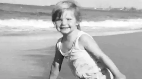 Grimmer family A black and white photo of a blonde girl in a swimsuit on a beach