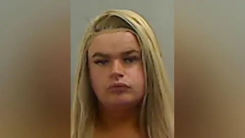 Cleveland Police Mugshot of Watkin. She has long blonde hair, a full face of make up and piercings above and below her mouth.