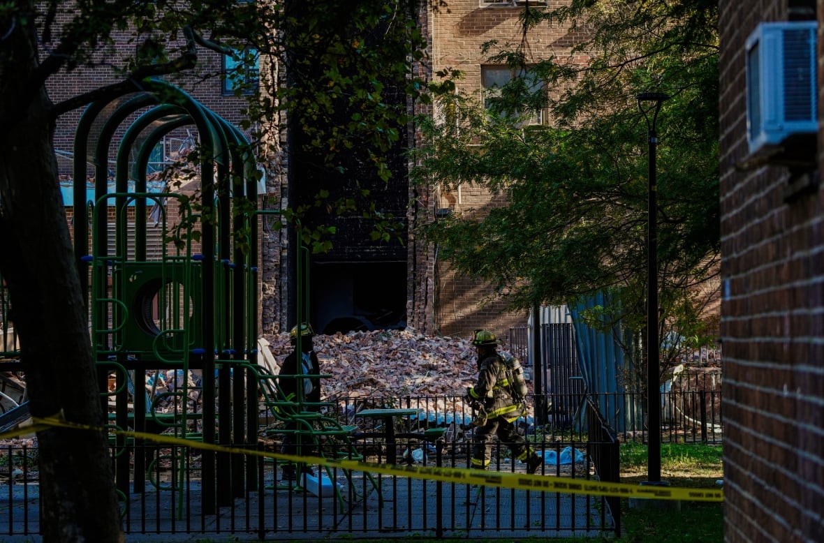 Firefighters are seen through next to a pile of bricks on the ground level of a highrise.