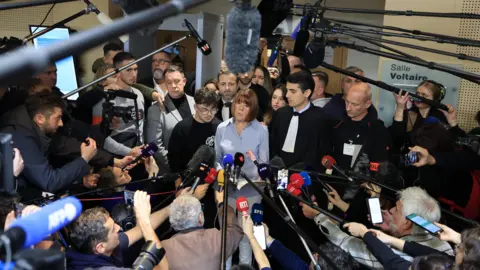 EPA Gisèle Pelicot framed at the centre of a dramatic wide-angle shot inside the courthouse, with a huge crowd of journalists surrounding her with microphones