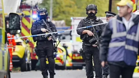 PA Media Armed police at the scene, with police vehicles in the background.
