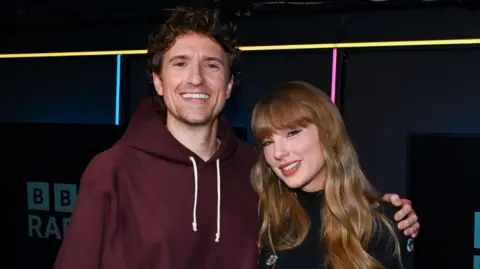 Greg James with his arm around Taylor Swift in the BBC Radio 1 studio