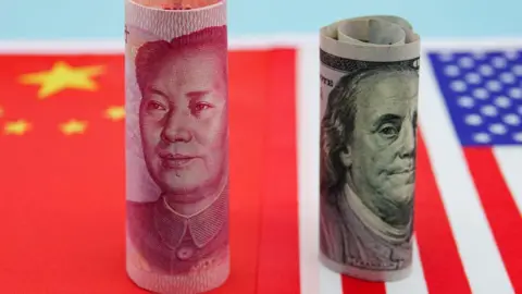 Getty Images Banknotes from China and US are rolled up and standing upright on flags of both countries