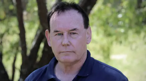 Australian Broadcasting Corporation Ricki Nash, Cheryl's brother, poses for a photo in a navy polo tee