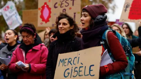 Reuters Women demonstrate outside the courthouse in Avignon, holding placards in support of Gisèle Pelicot. One at the front of the image holds a cardboard handwritten sign which says in French: "Thank you, Gisèle"