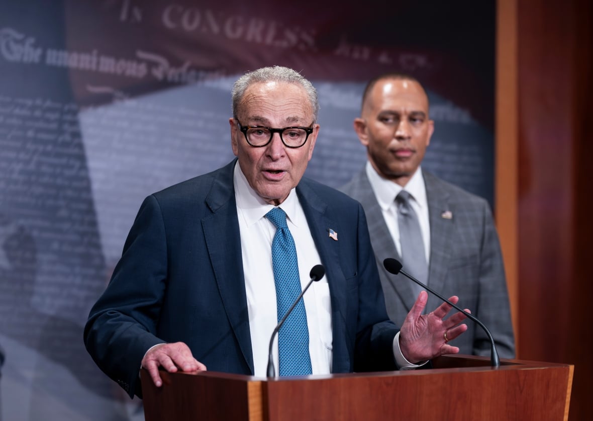 Two men in suits speak at  a  podium