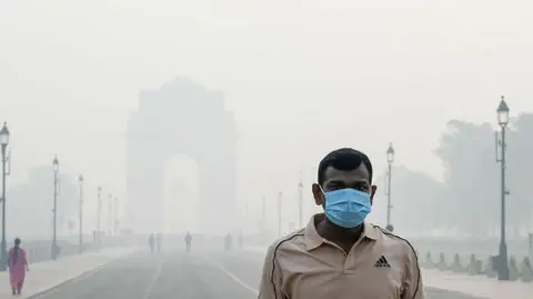 Hindustan Times via Getty Images A man wearing a beige t-shirt and a blue mask walks in front of the India Gate in Delhi on 21 October 2025