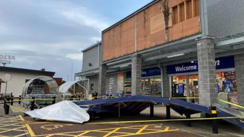 A large metal shop sign lying in a carpark after falling off the building above